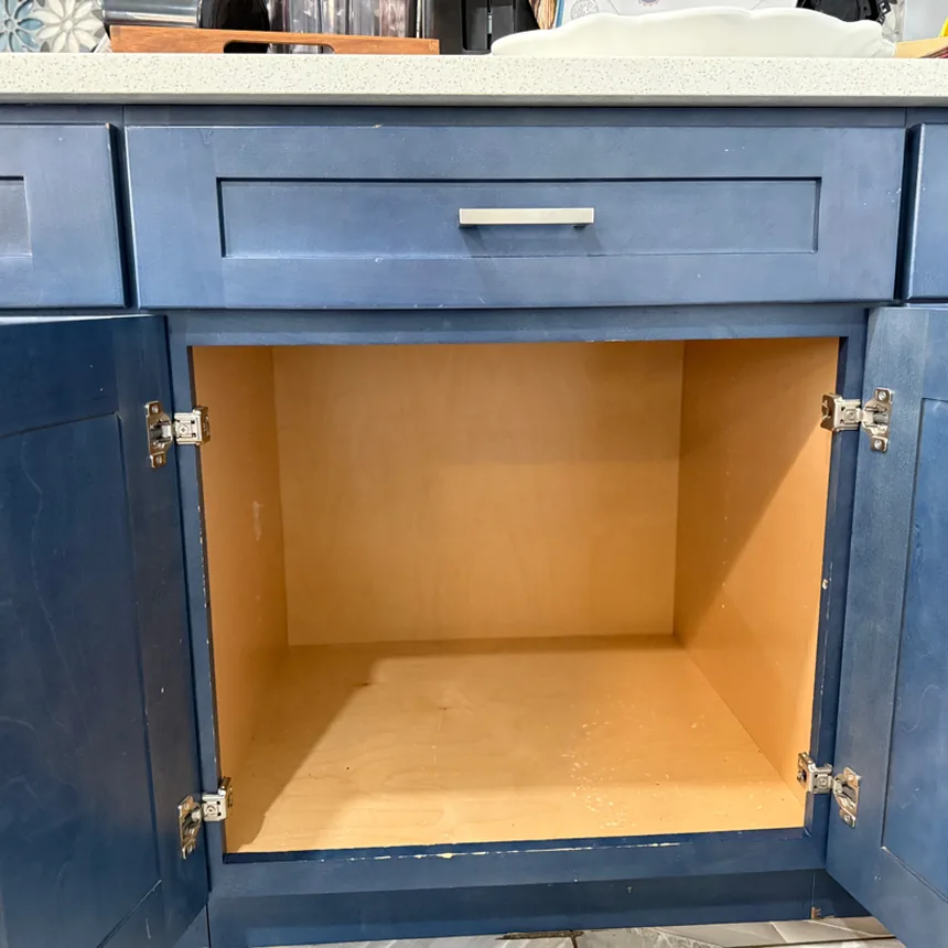 Empty base cabinet in a navy blue kitchen with the doors open
